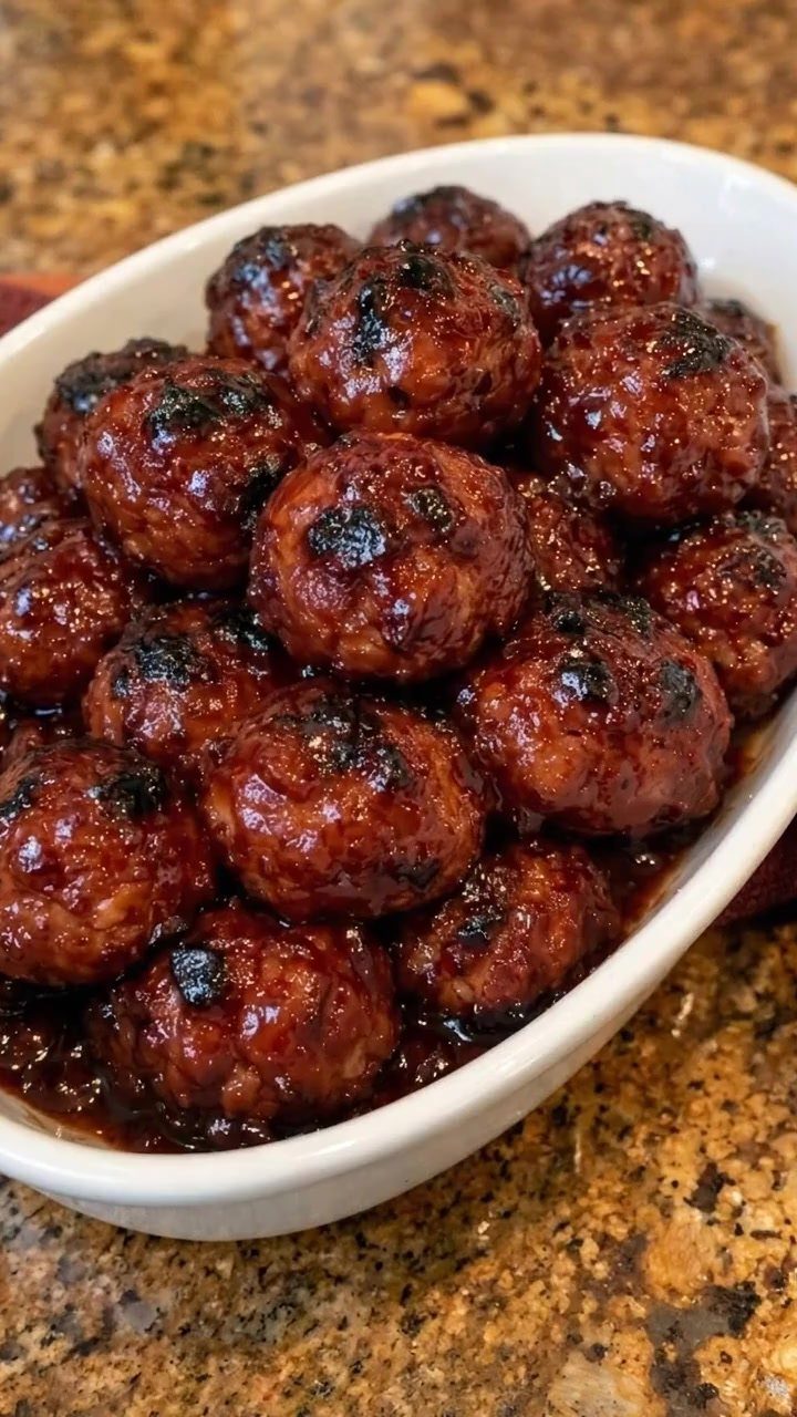 Glazed BBQ meatballs served in a white oval ceramic dish on granite.