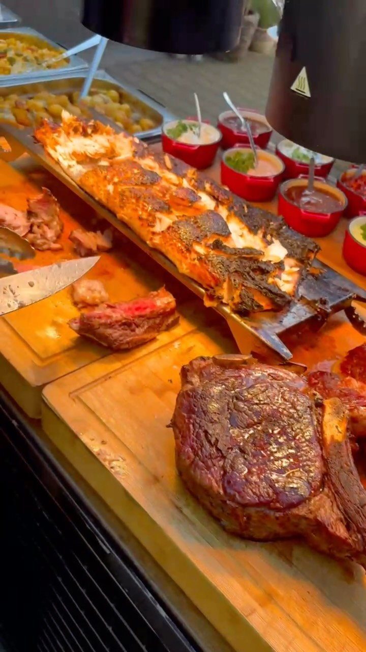 Grilled meats and sauces arranged on wooden boards for a buffet style spread.