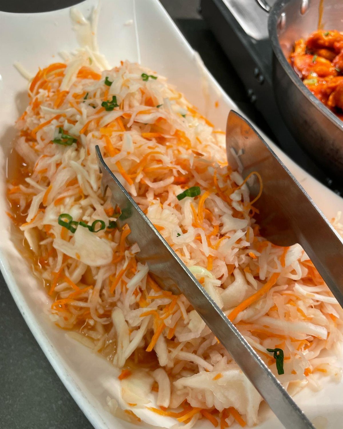 Coleslaw with shredded cabbage and carrots in a white platter with metal tongs.