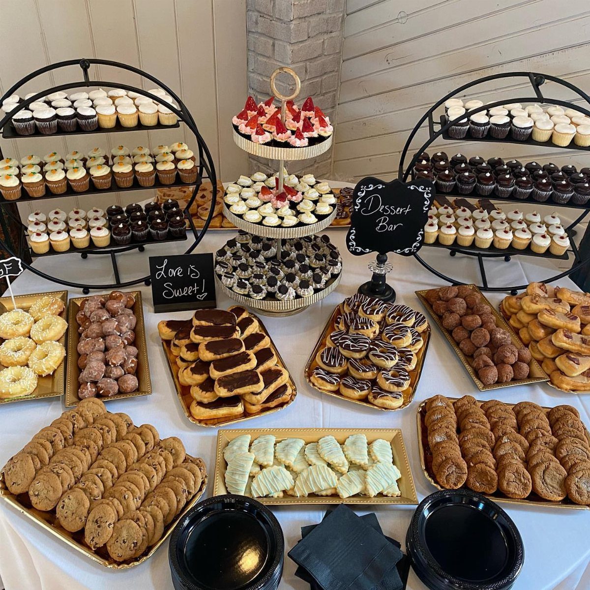 Dessert buffet table featuring cupcakes, donuts, cookies, and eclairs on gold trays.