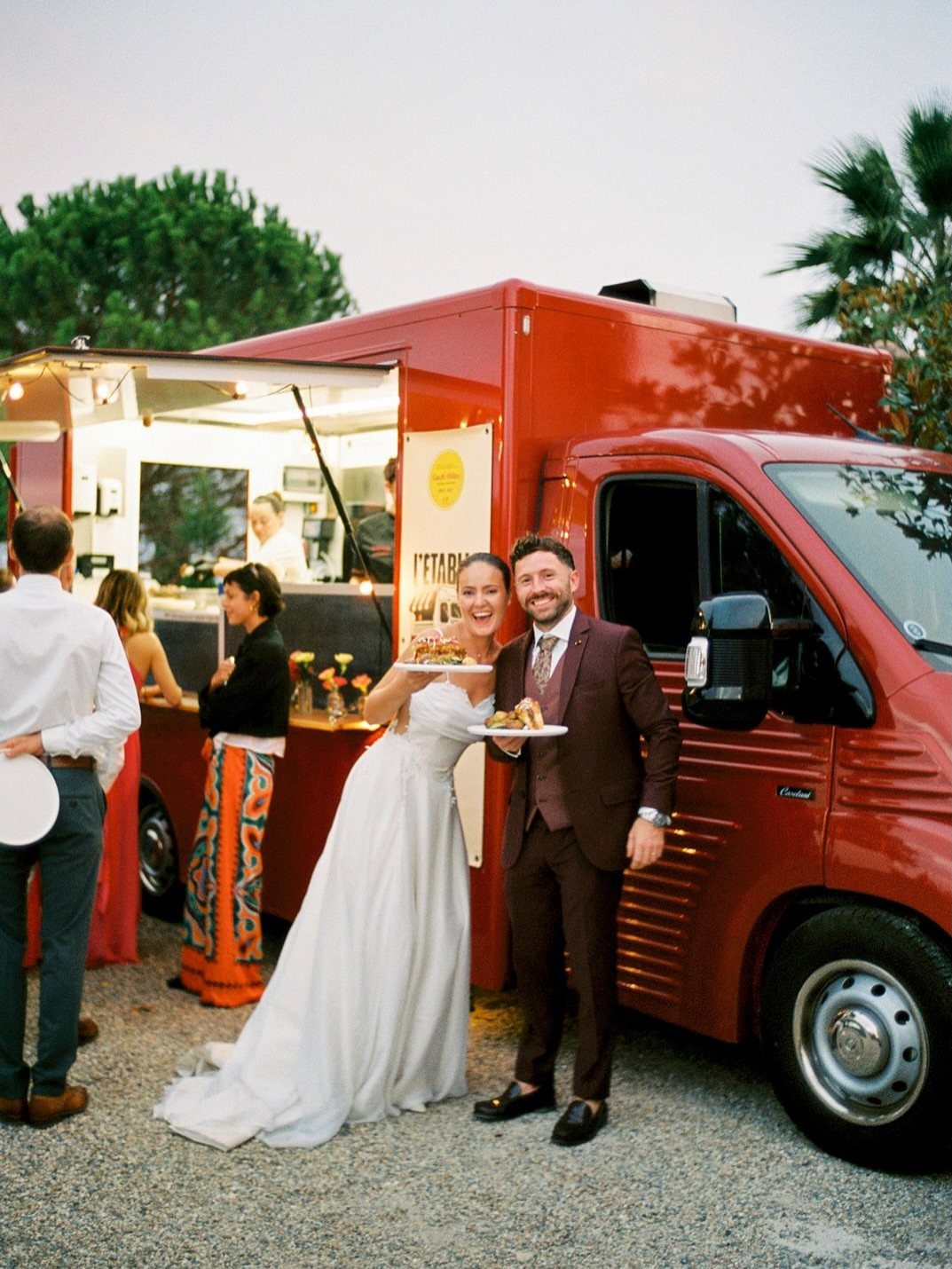 Bride and groom holding plates of food in front of a red food truck.