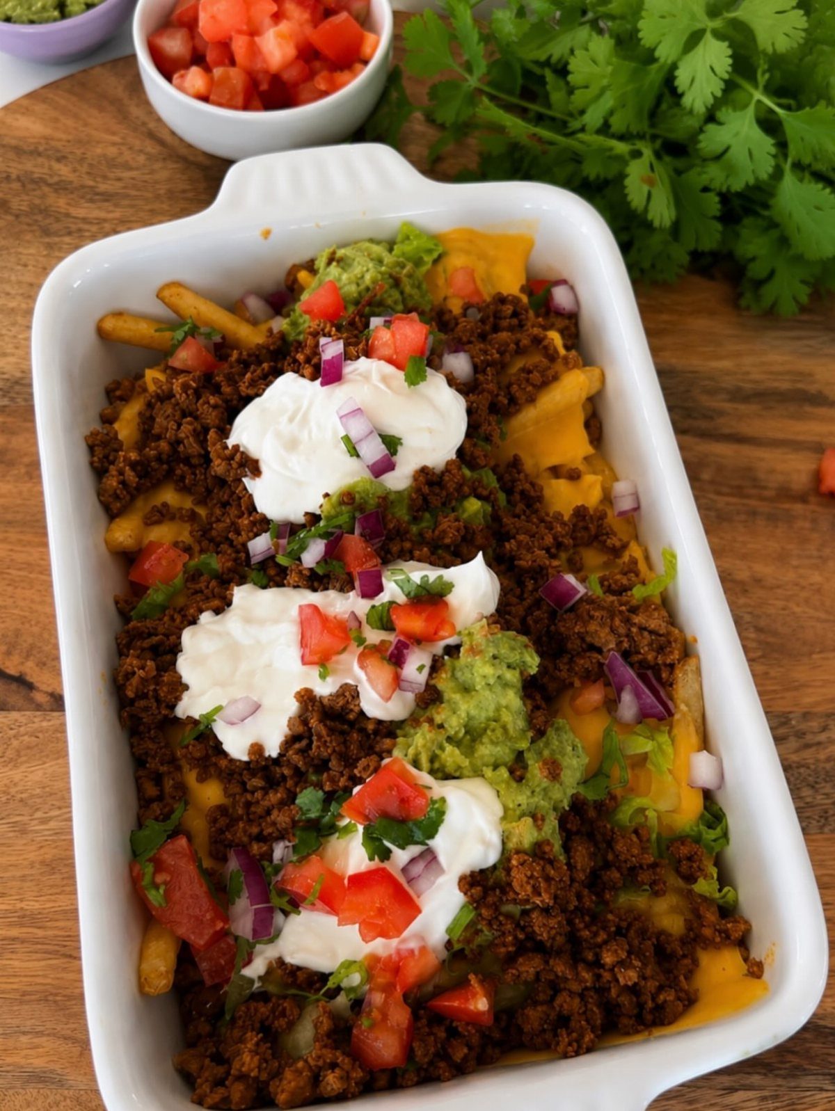 Loaded fries with meat, cheese, and toppings in a white ceramic baking dish.