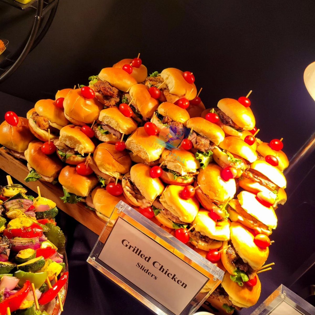 Grilled chicken sliders and vegetable skewers arranged on a buffet catering platter.