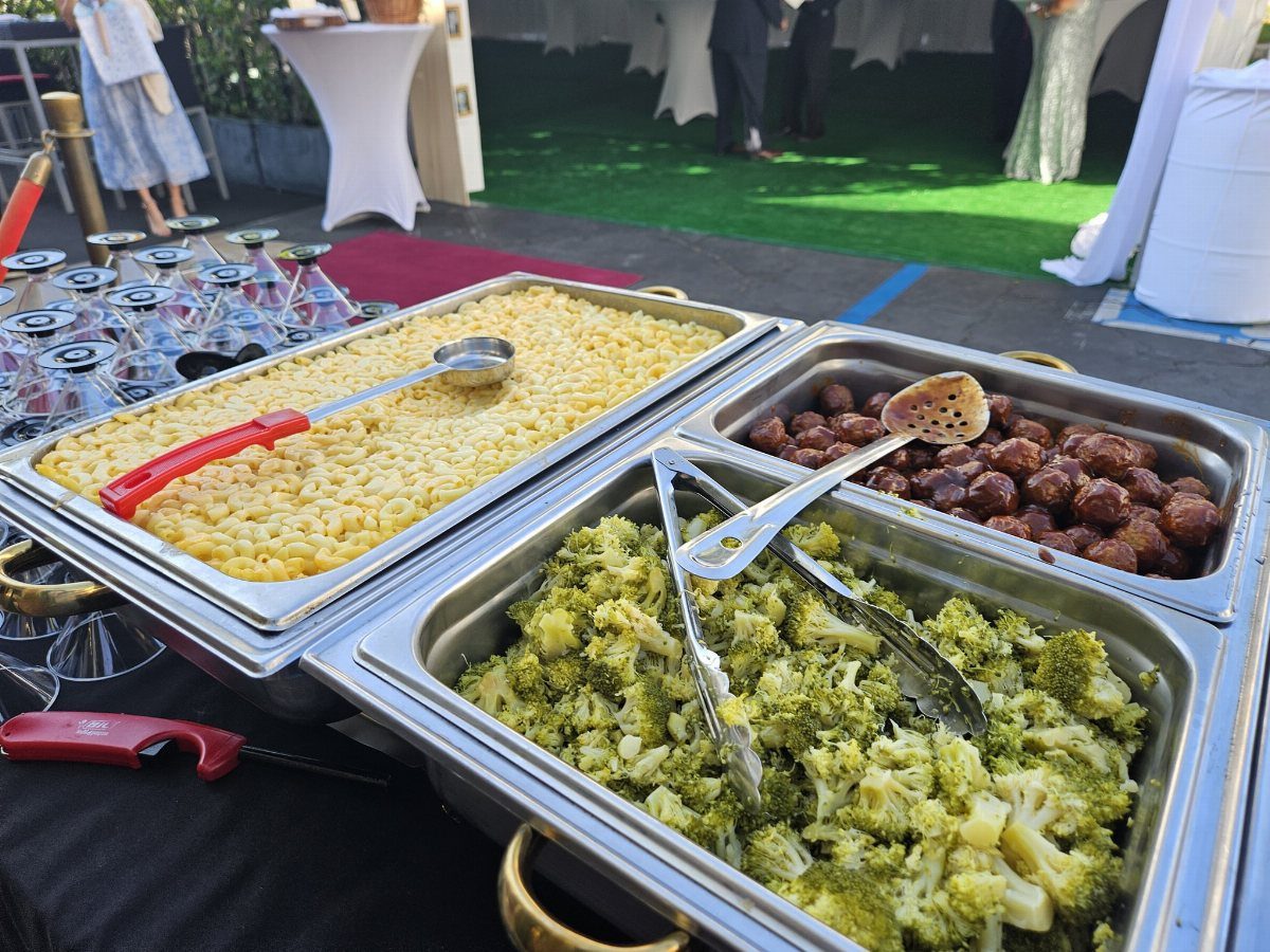 Macaroni and cheese, meatballs, and broccoli served in silver buffet chafing dishes.