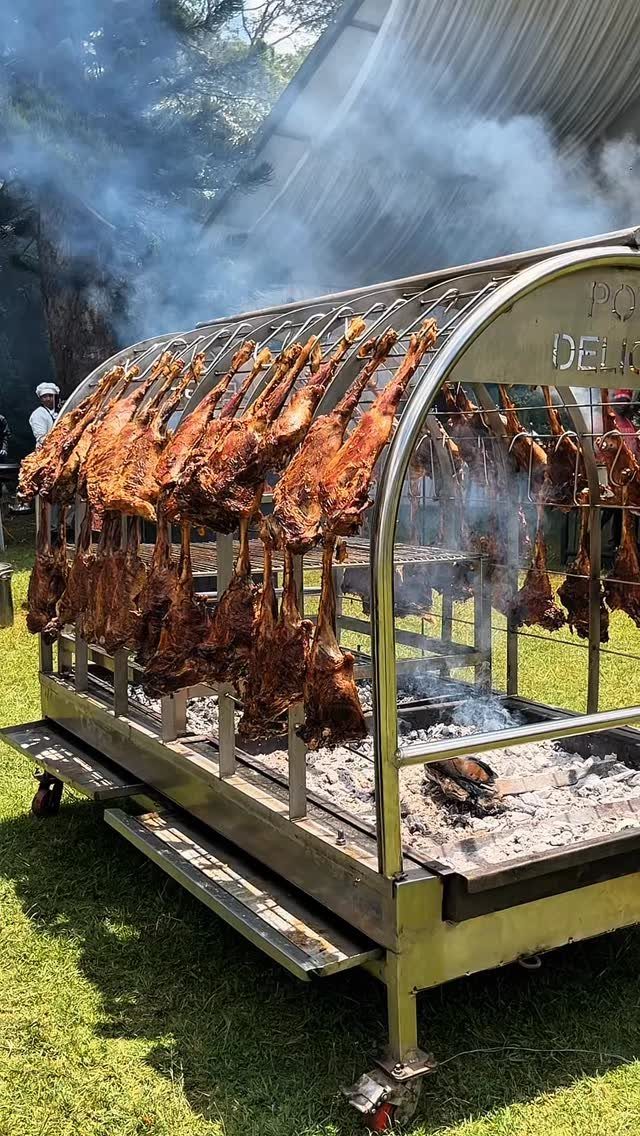 Large stainless steel outdoor grill with roasted meats hanging over hot coals.
