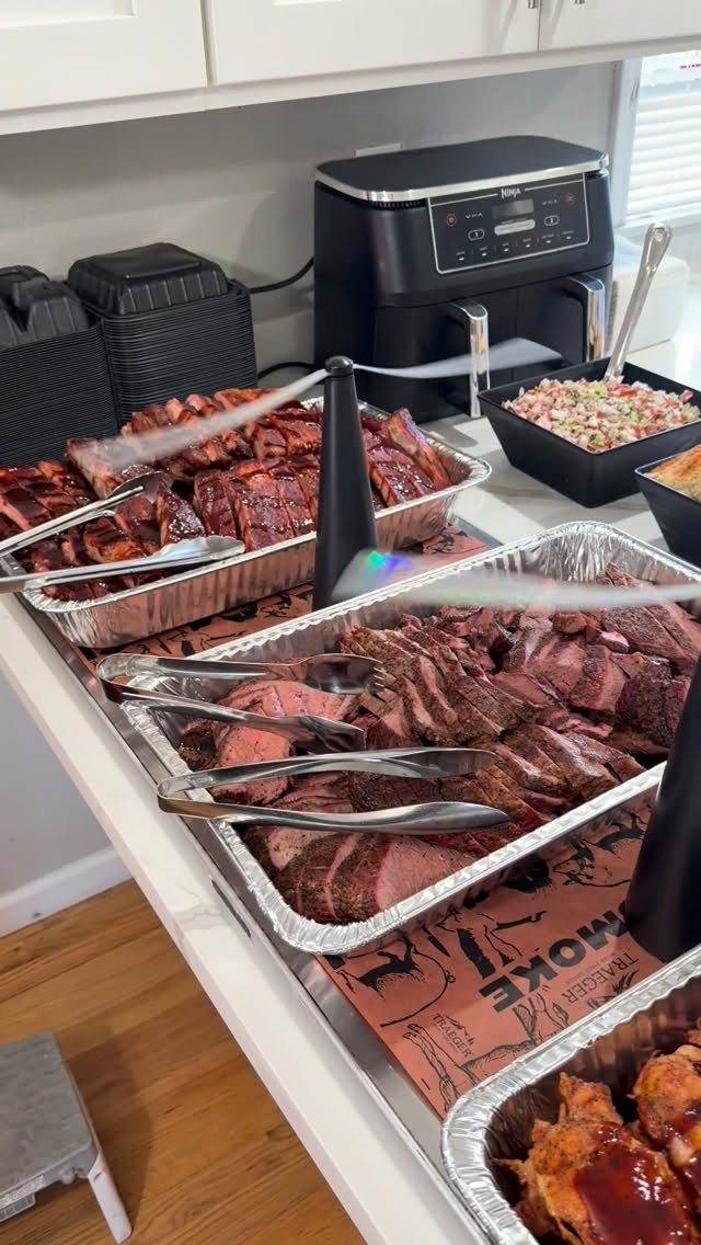 Smoked brisket and ribs in aluminum trays on a white buffet counter.