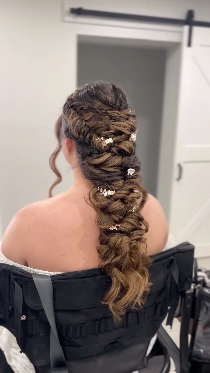 Woman's long brown curly hair styled in a textured braid with floral pins.