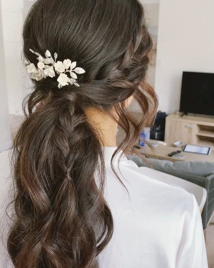 Wavy brown hair in a braided ponytail with a white floral hair accessory.