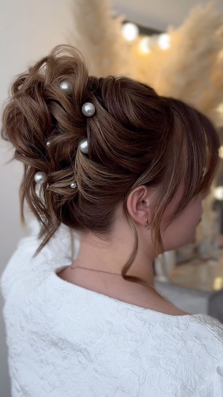 Textured brown hair updo bun decorated with white pearl pins and lace dress