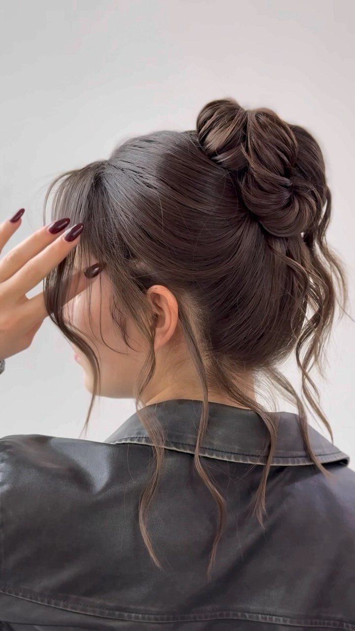 Woman with brown hair in a textured high bun and loose curling tendrils