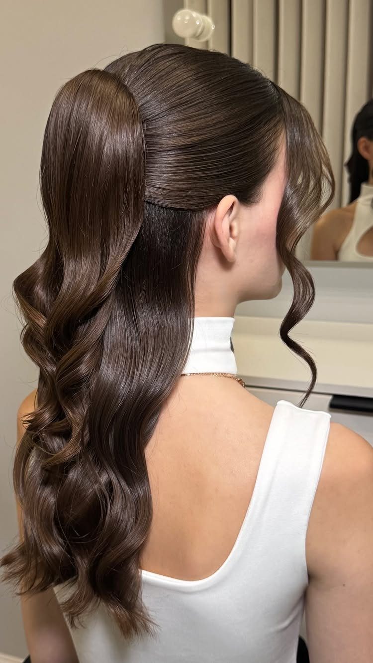 Woman with a high voluminous brown ponytail and curls wearing a white top