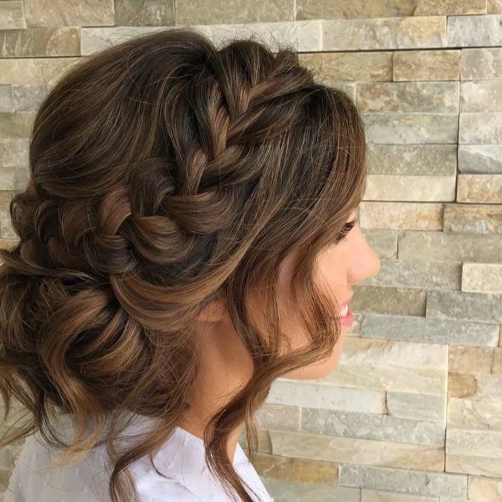 Woman with brown hair in a braided updo with loose face-framing curls.