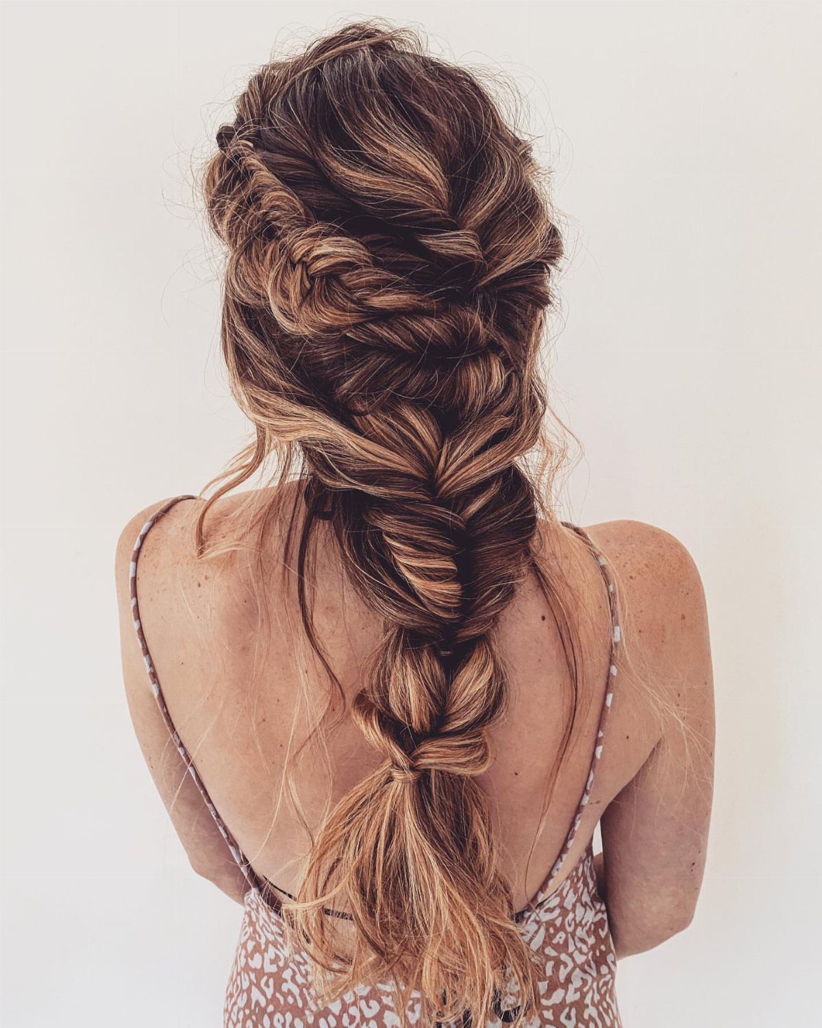 Woman's brown hair styled in a textured, voluminous fishtail braid from behind.