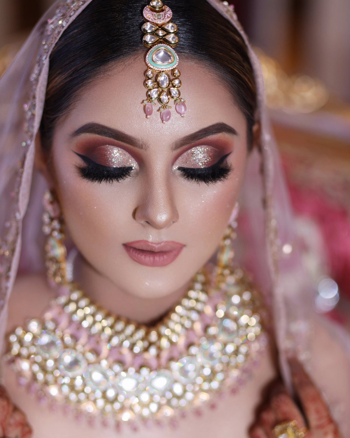 Woman with shimmering gold cut crease bridal eye makeup and traditional Indian jewelry.