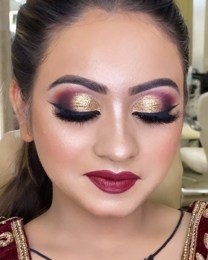 Woman with gold glitter and burgundy bridal eye makeup and deep red lips.
