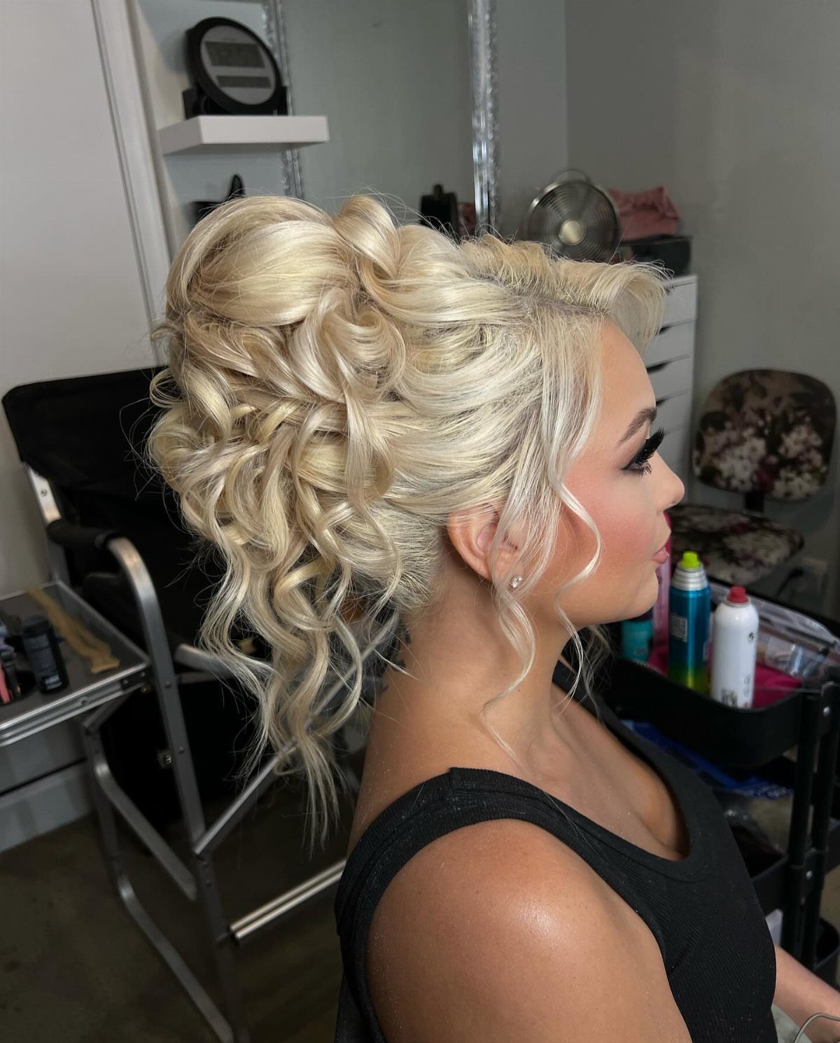 Blonde woman with a voluminous curly updo hairstyle in a salon setting.