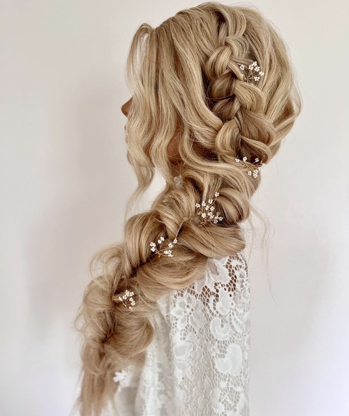 Blonde hair styled in a loose side braid with small white floral pins
