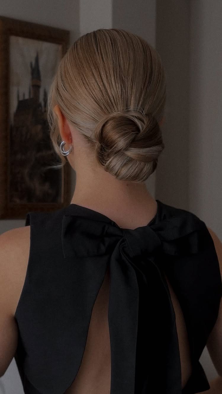 Blonde hair styled in a polished low bun with a black bow dress