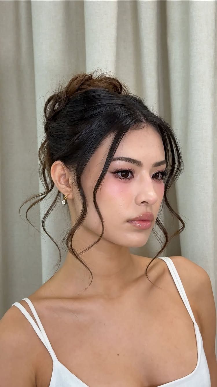 Woman with a high messy bun and curly face-framing strands against beige curtains