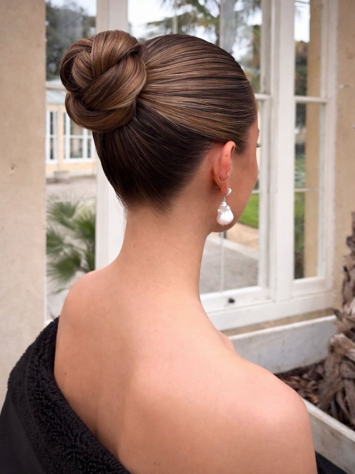 Woman with brown hair styled in a polished high bun and pearl earring