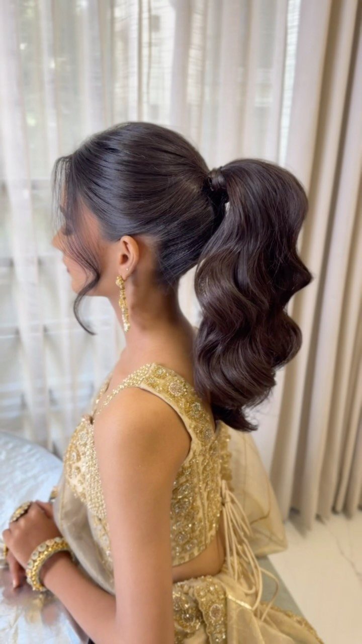 Woman with a high voluminous wavy ponytail wearing a gold embroidered dress