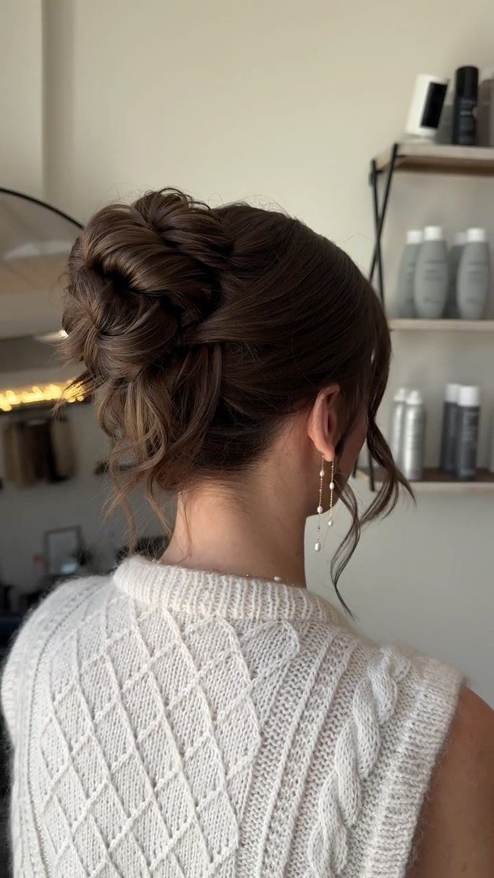 Woman with a textured brown hair updo and loose tendrils wearing white sweater