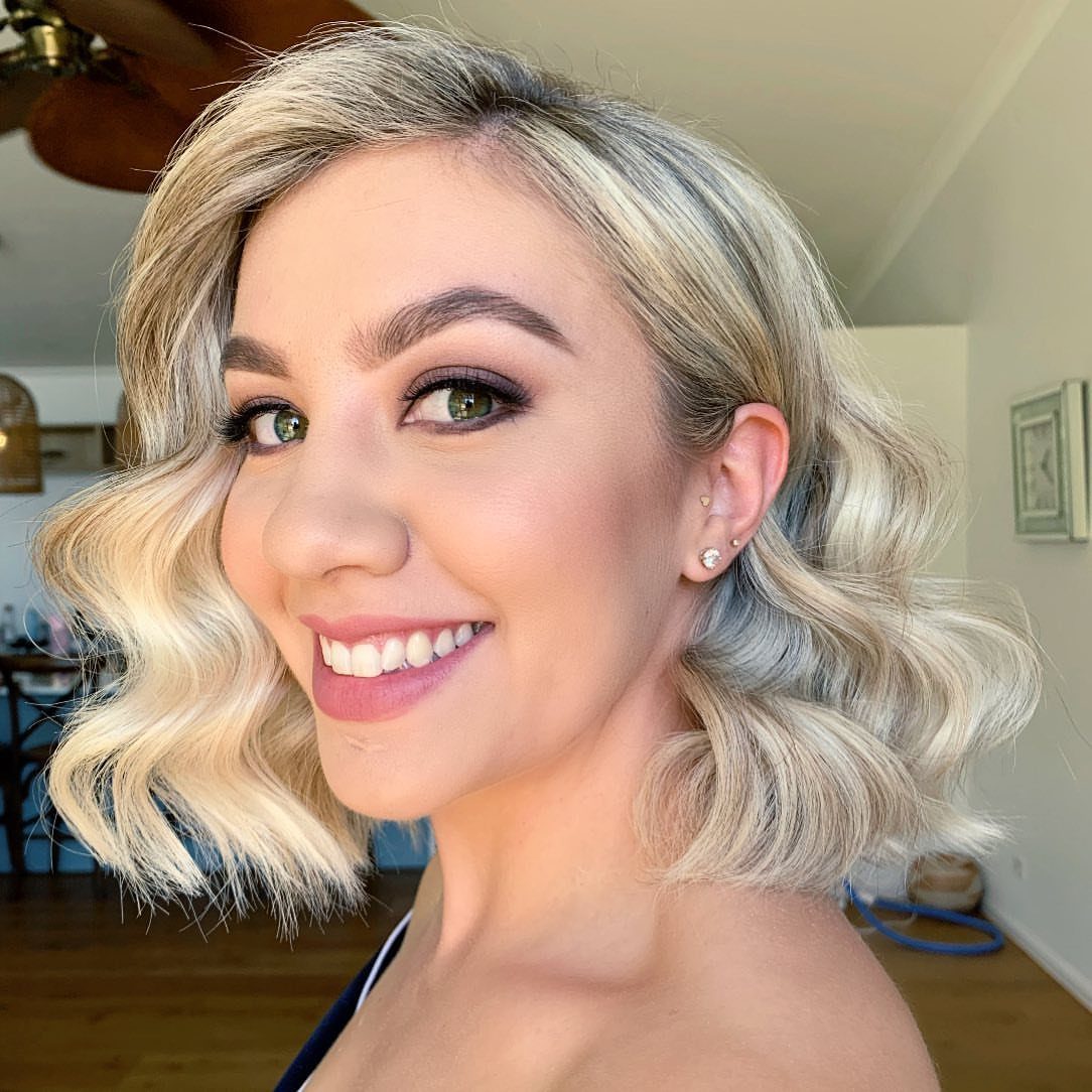 Woman with a blonde wavy bob hairstyle smiling in a bright room