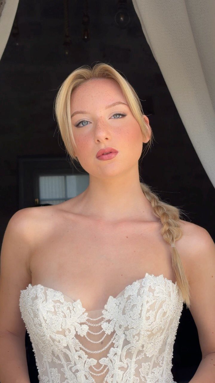 Blonde bride with natural makeup and braided hair wearing a white lace gown.