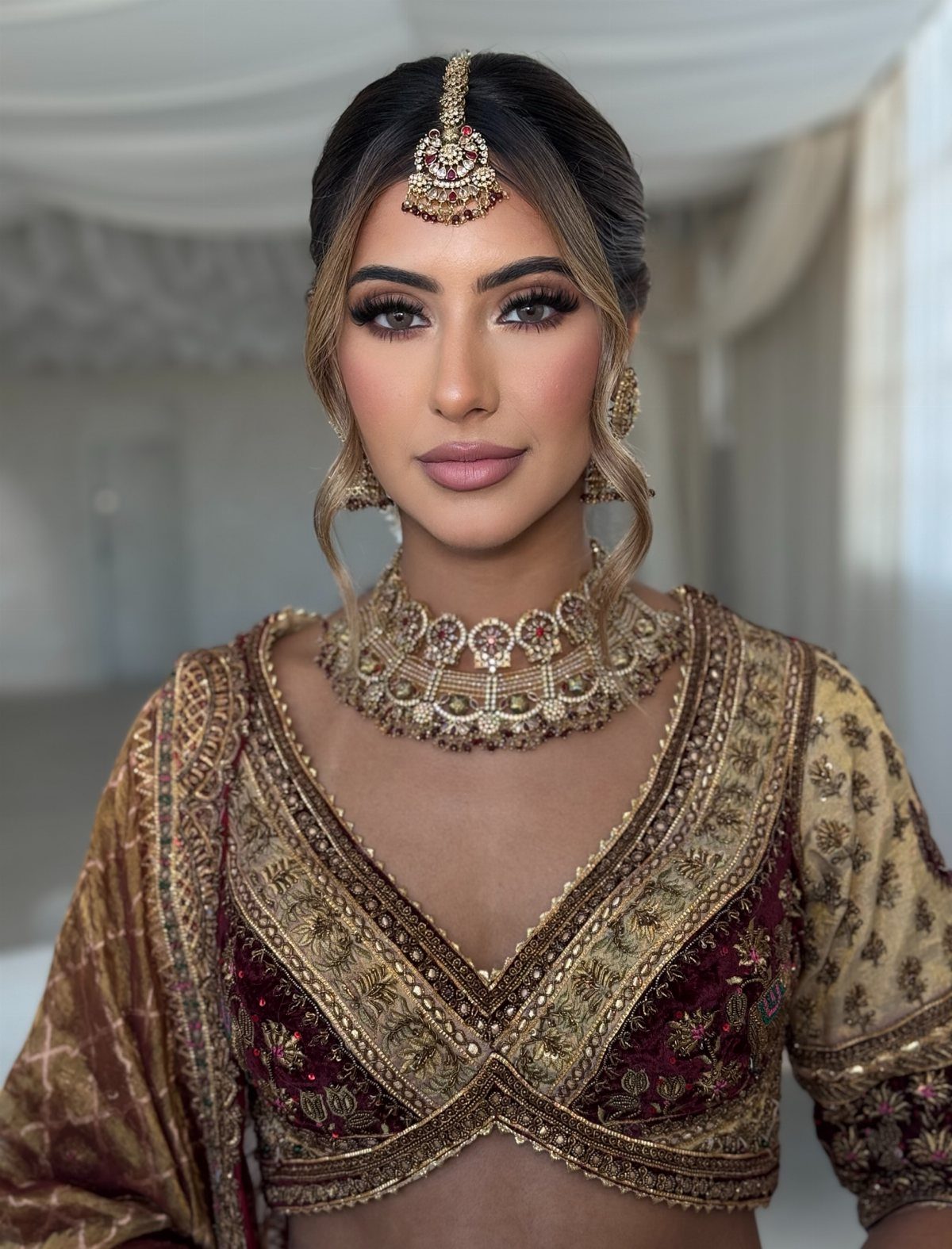 Woman in traditional Indian bridal attire with glamorous makeup and gold jewelry.