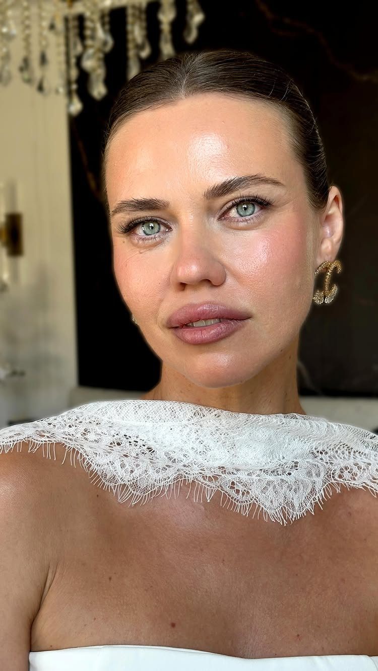 Woman with glowing dewy skin wearing a white lace bridal dress and gold earrings