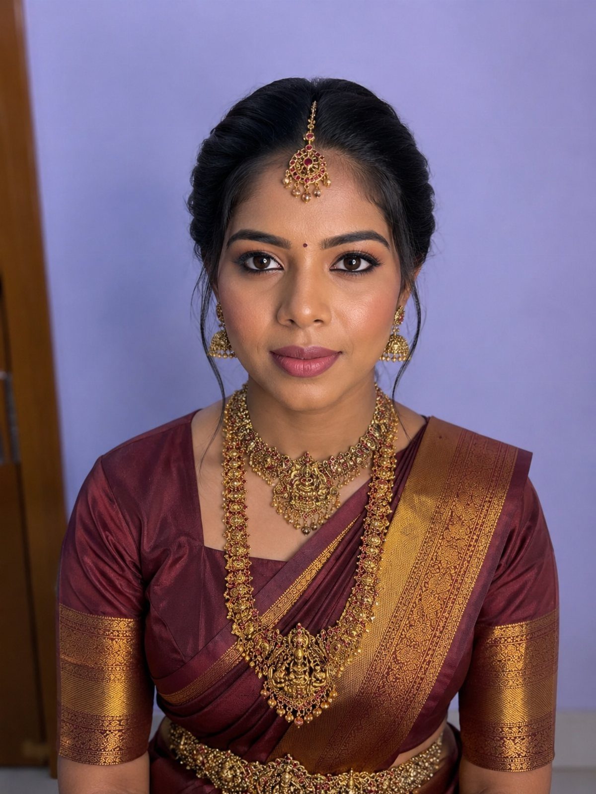 Woman in maroon saree and gold jewelry with polished natural bridal makeup.