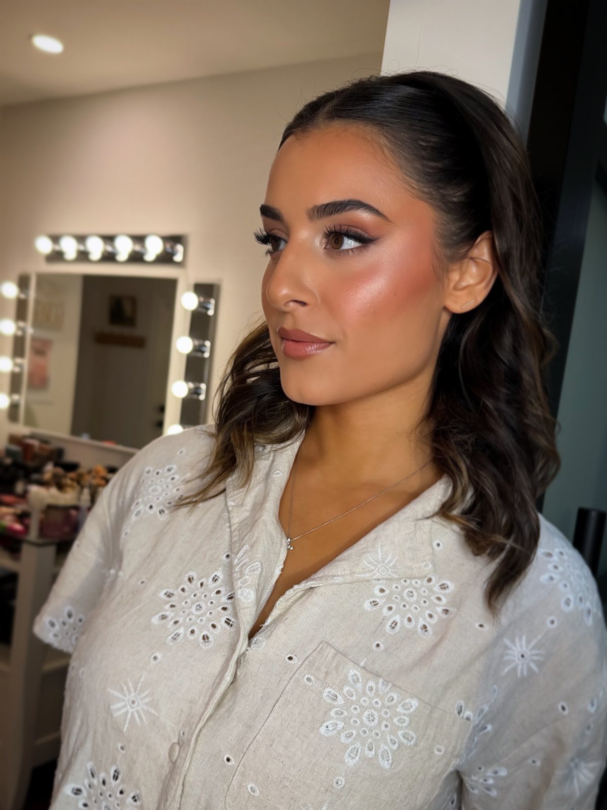 Woman with warm-toned makeup and wavy brown hair posing in a makeup studio