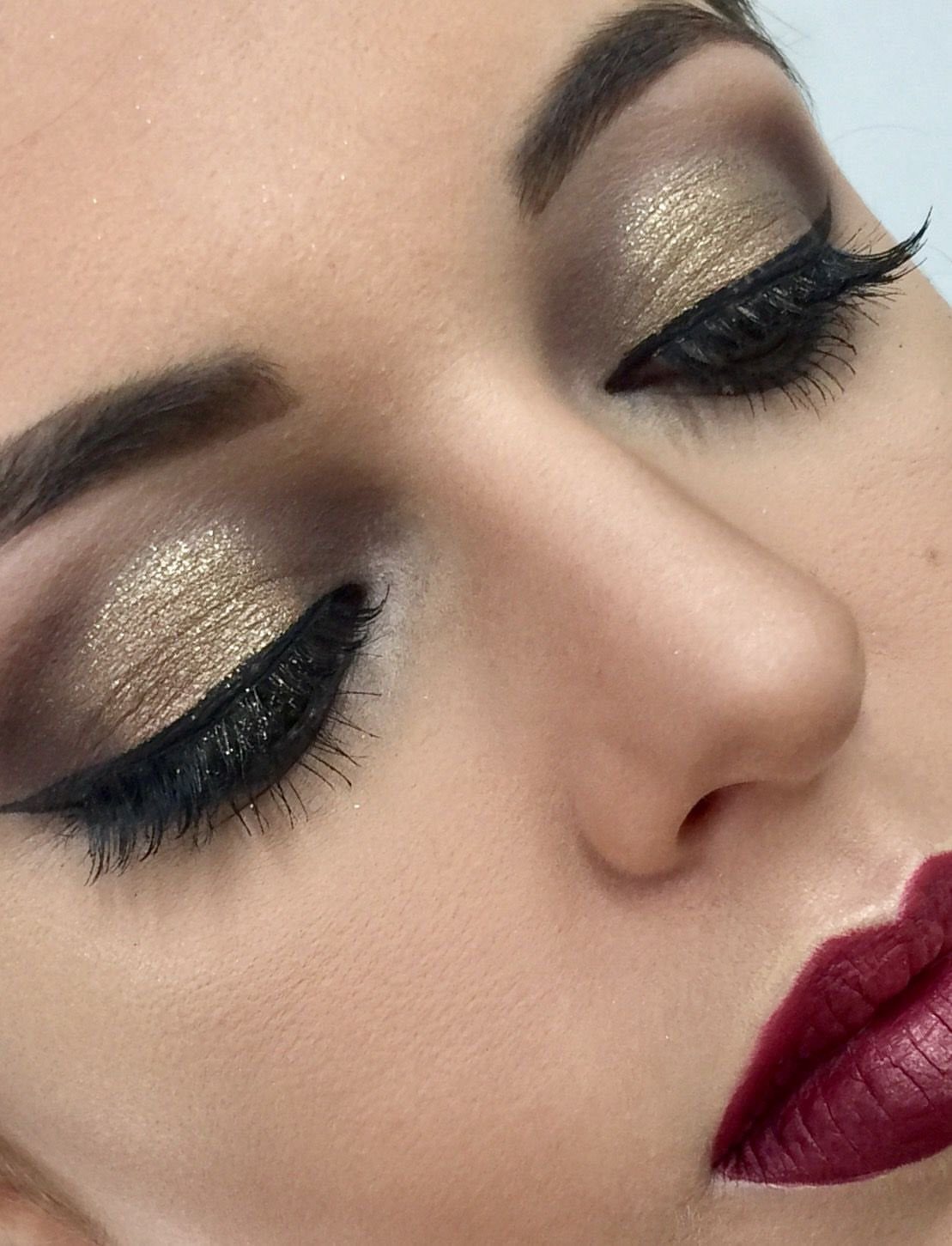 Woman with gold shimmer smoky eye makeup and deep burgundy matte lipstick.
