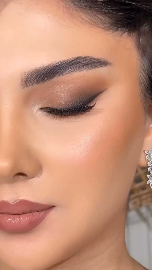 Woman with glam makeup featuring winged eyeliner, shimmering eyeshadow, and mauve lips.