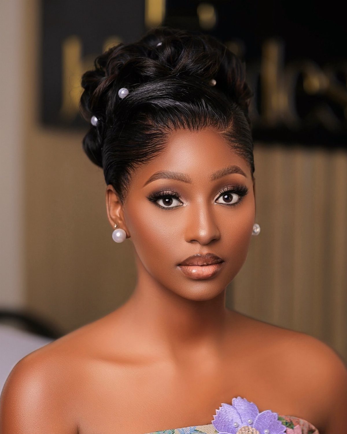 Woman with luminous bronzed makeup and an elegant pearl-adorned updo posing for portrait