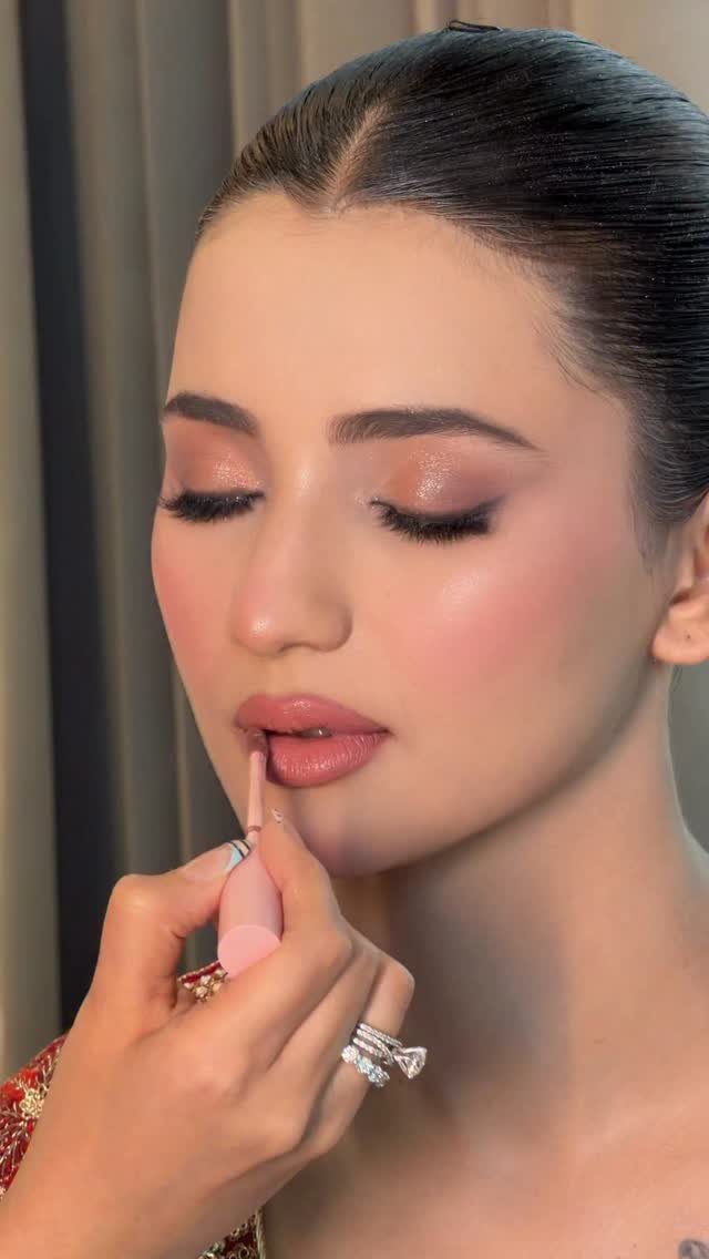 Woman receiving lipstick application with shimmering eyeshadow and glowing bridal makeup