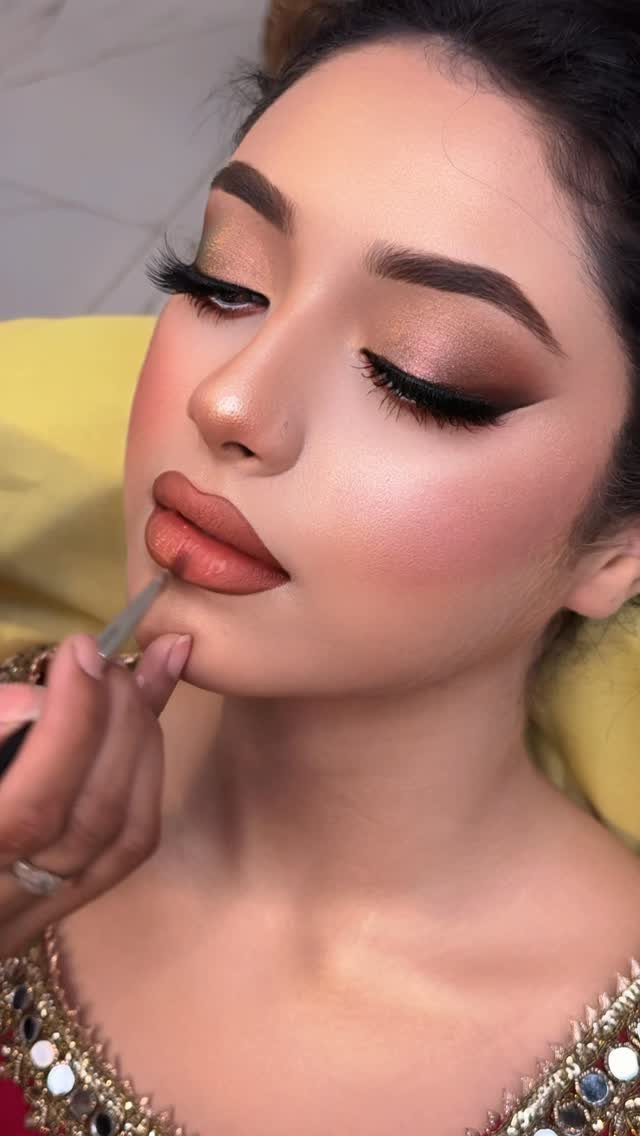 Woman with dramatic eye makeup and terracotta lips getting lipstick applied with a brush