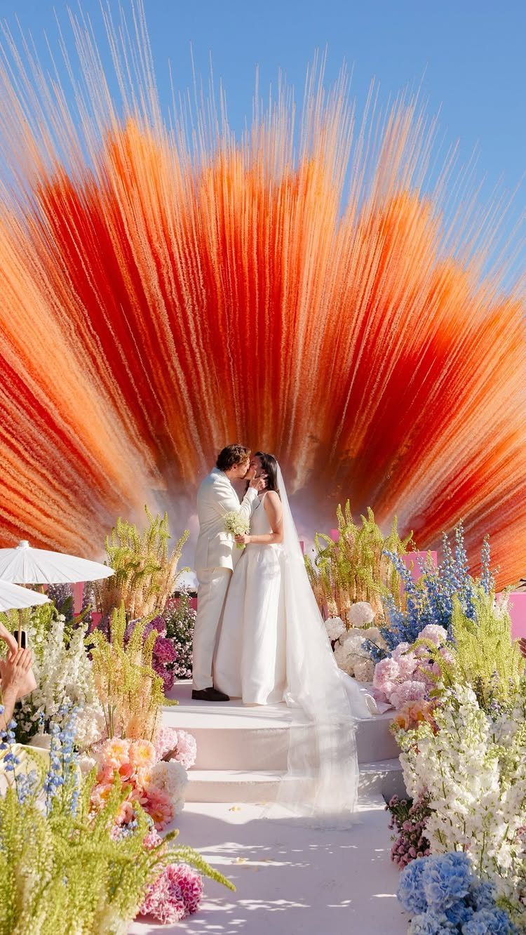Bride and groom kissing at an altar with a large orange fiber backdrop.