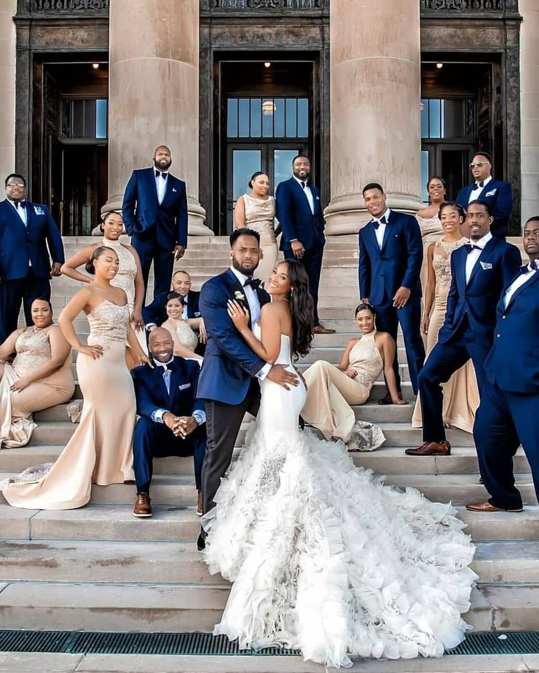 Bride and groom embracing on stone steps surrounded by their bridal party.