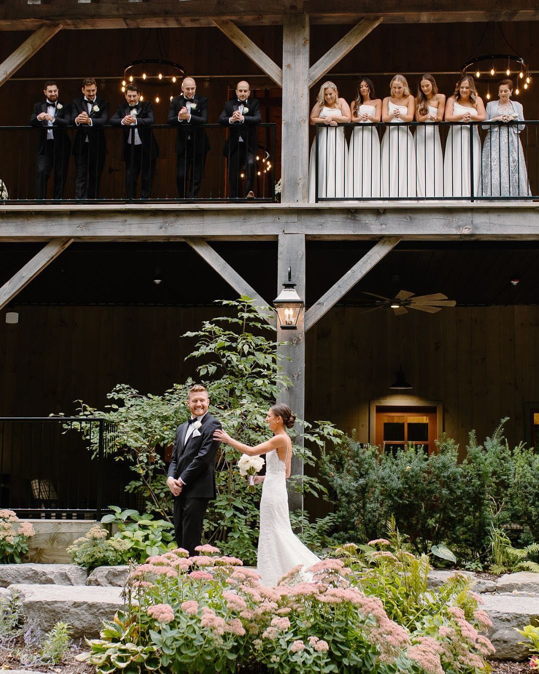 Bride and groom in a garden with bridal party watching from a balcony