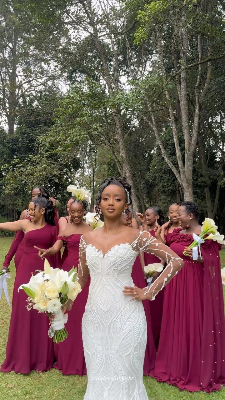 Bride in white lace gown with bridesmaids in burgundy dresses in a park