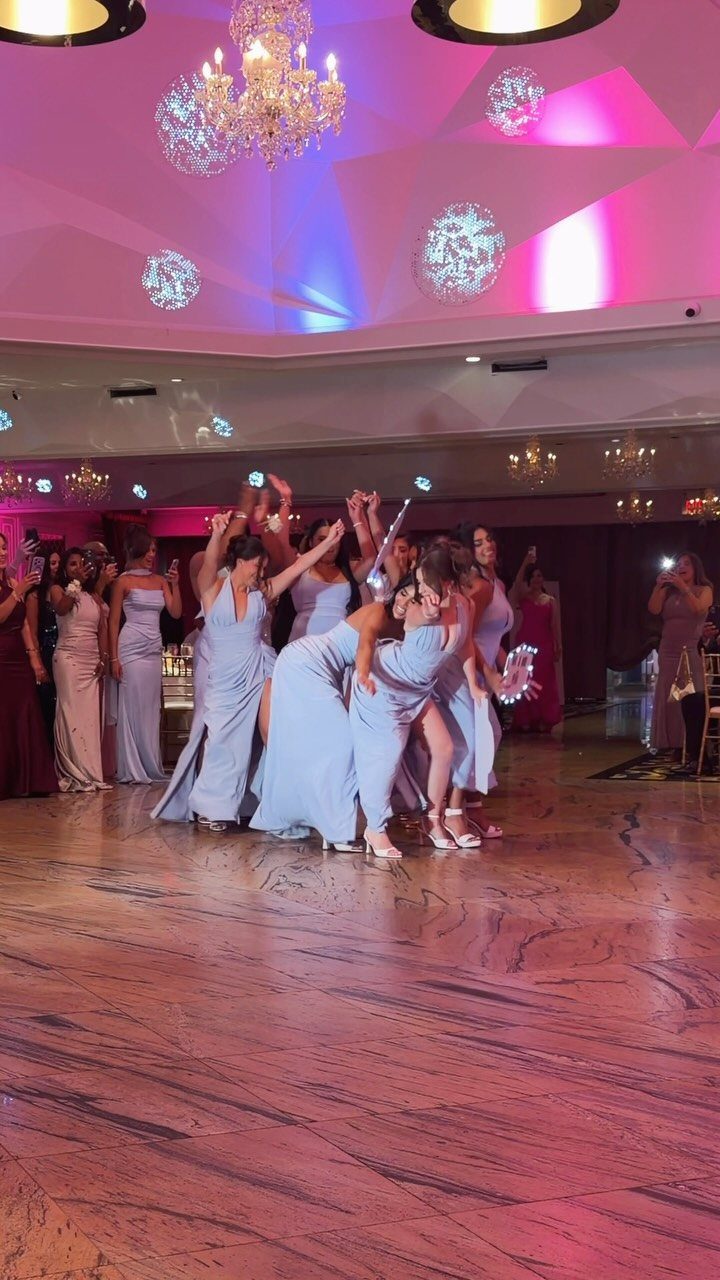 Bridesmaids in light blue gowns posing playfully on a ballroom dance floor.