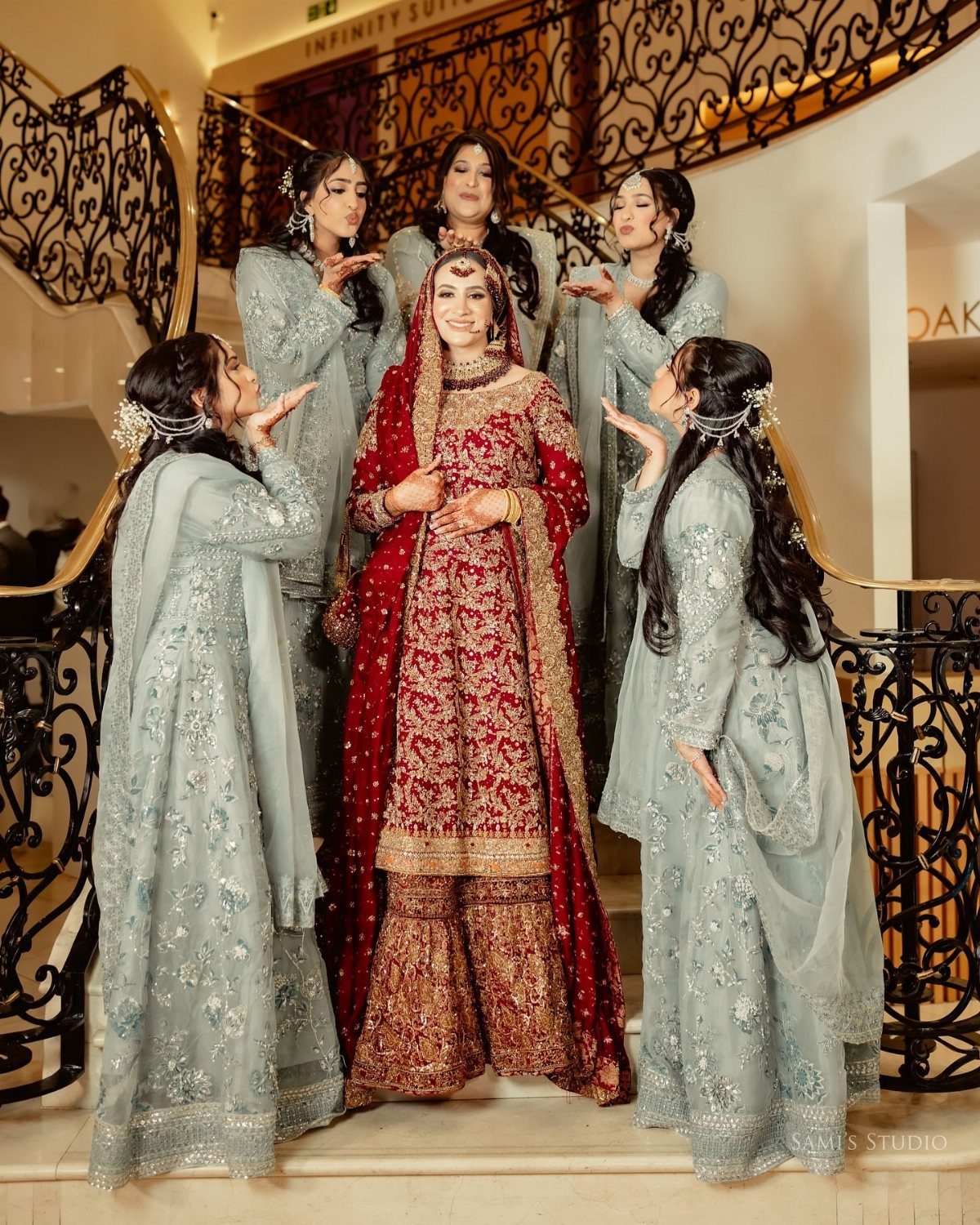 Bride in red traditional dress surrounded by bridesmaids in light blue on stairs