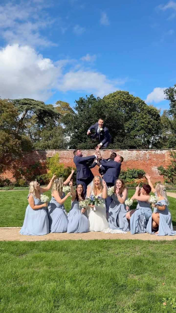 Groomsmen lifting the groom in the air while the bride and bridesmaids cheer.
