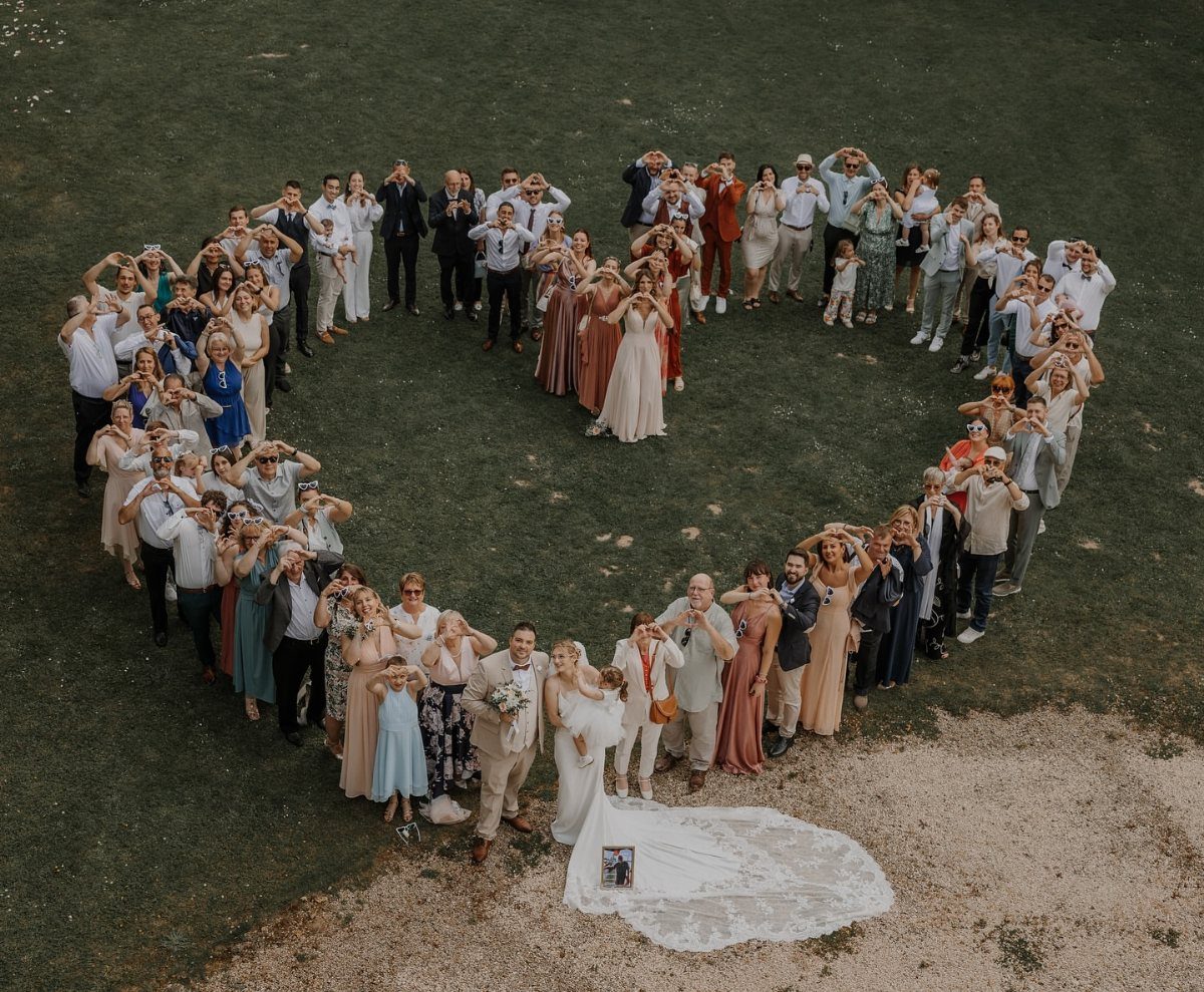 Wedding party and guests arranged in a heart shape around a bride and groom.