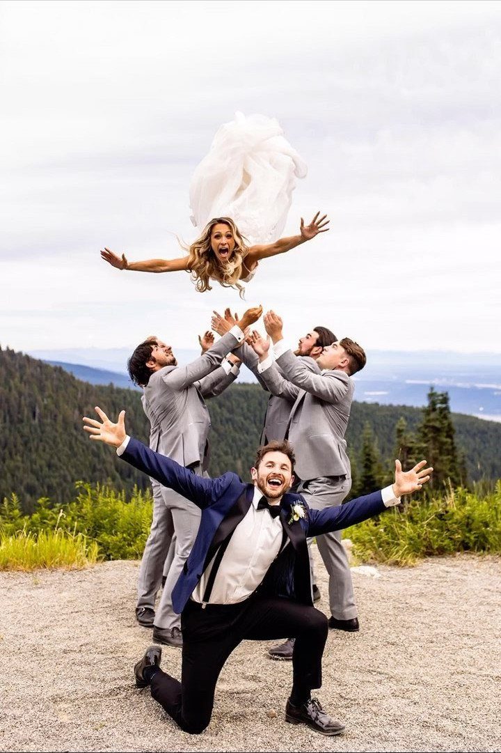 Bride tossed in the air by groomsmen with groom kneeling in the foreground.