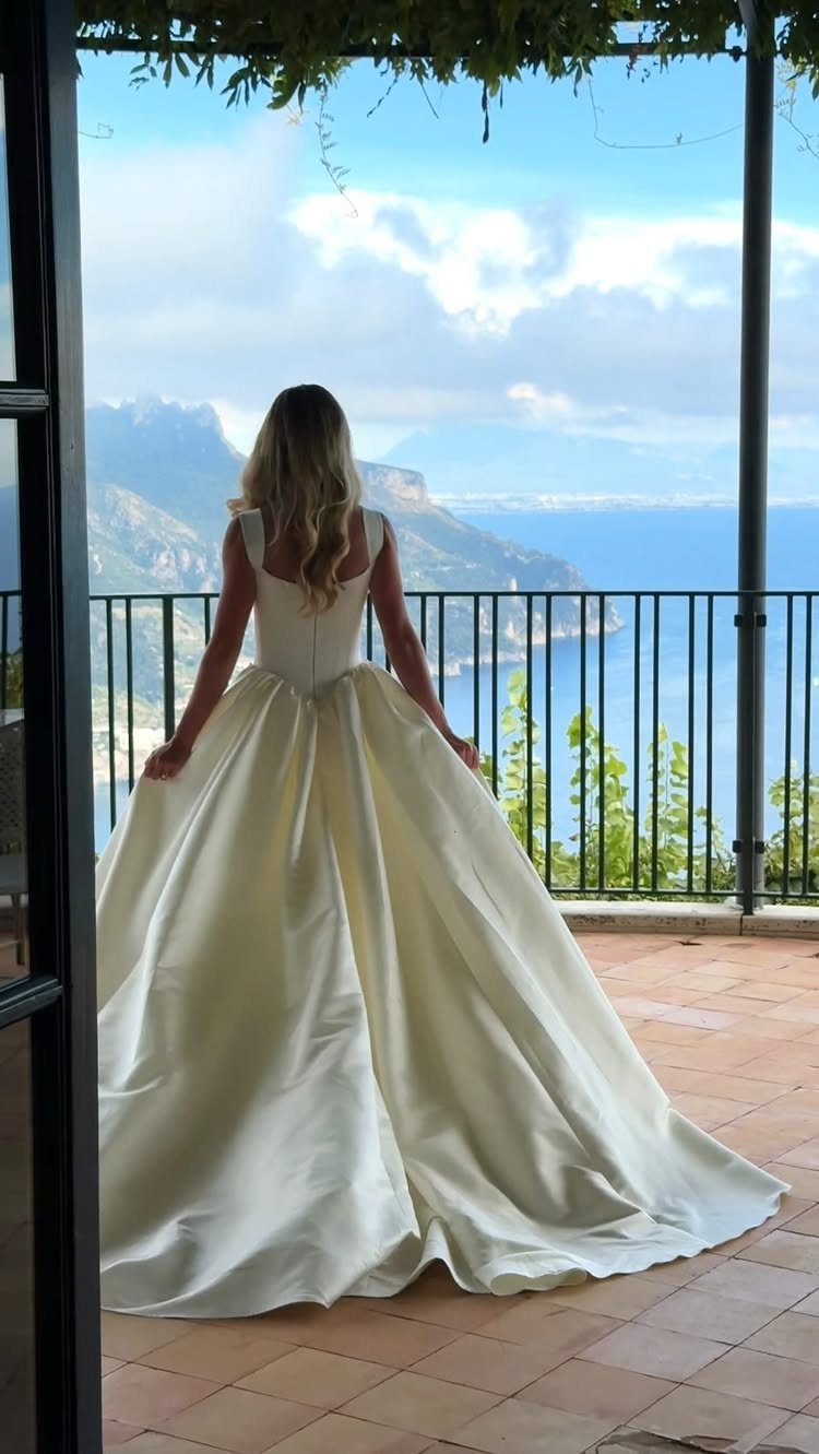 Bride in a white gown standing on a balcony overlooking a coastal landscape