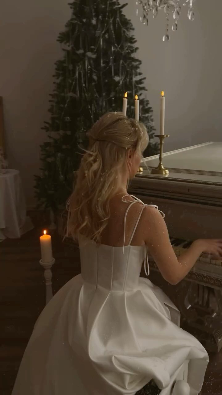 Bride in a white gown sitting at a piano with a Christmas tree behind.
