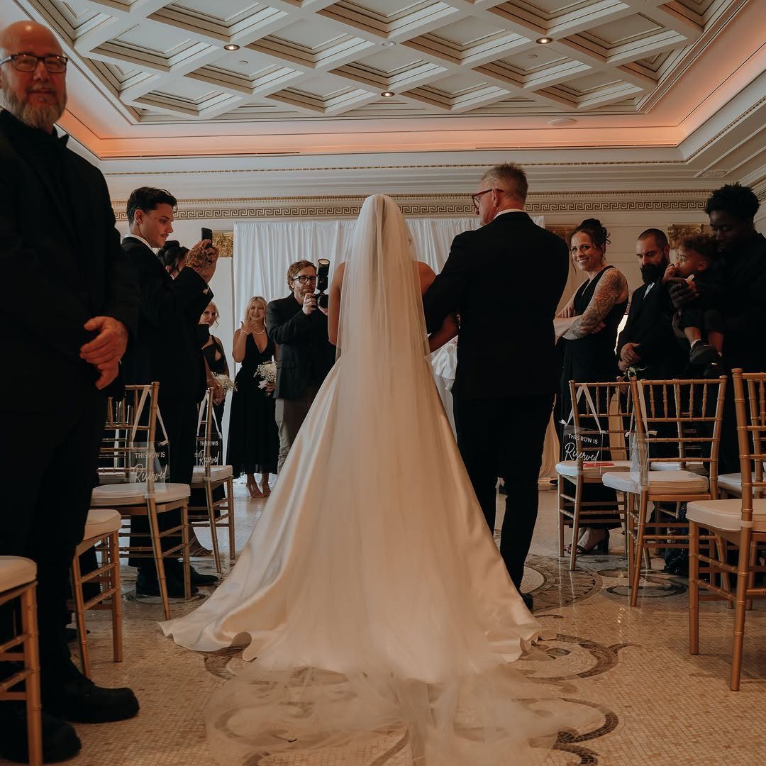 Bride in white gown and veil walking away down a wedding aisle.