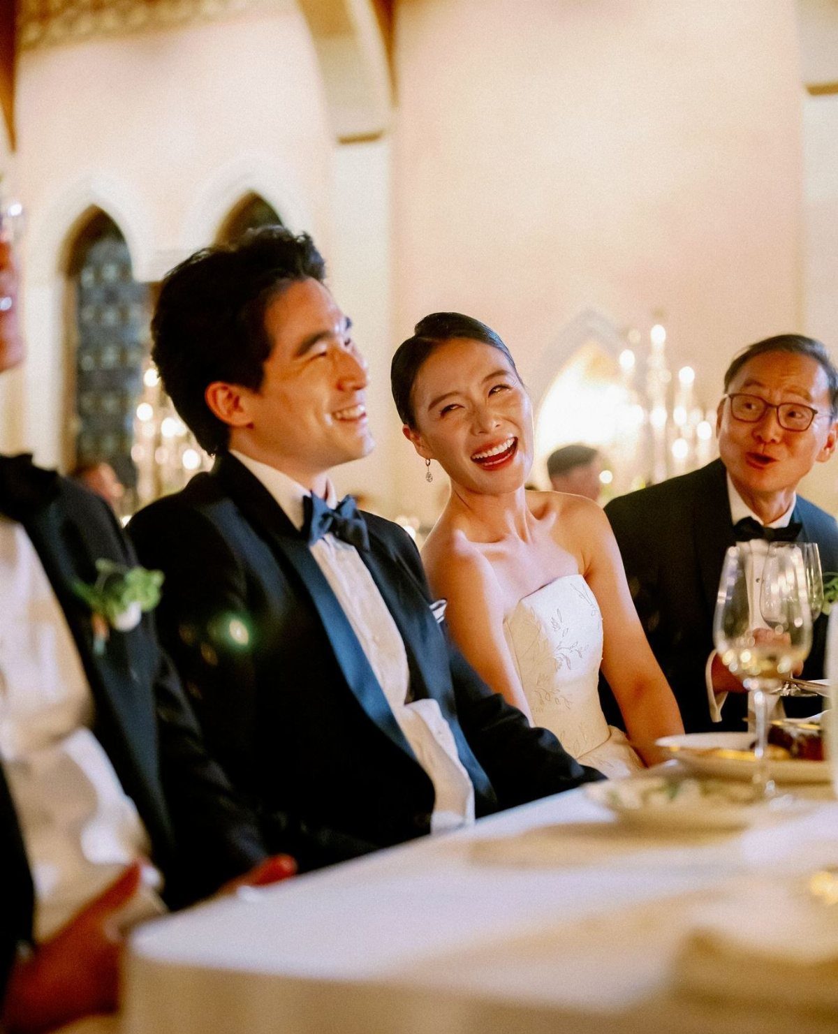 Bride and groom laughing joyfully while sitting at a wedding reception dinner table.